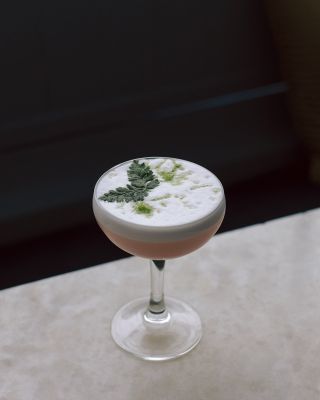 A frothy pink cocktail with a mint leave on top