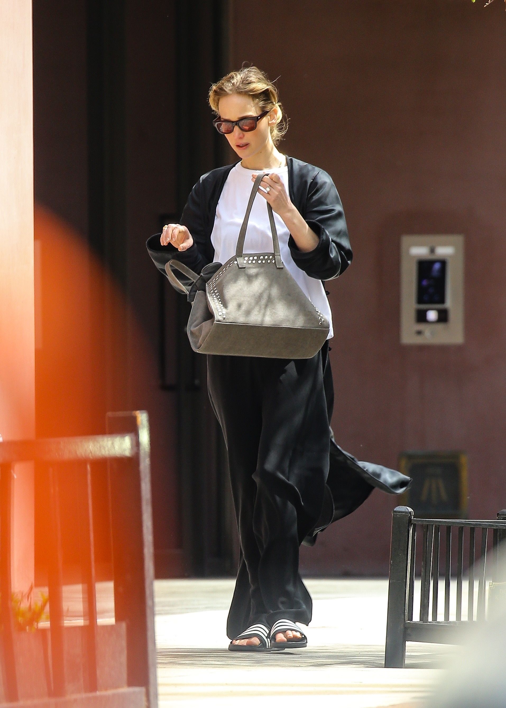 Jennifer Lawrence walks down the street in New York wearing black trousers with slides and a white t-shirt.