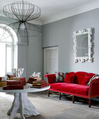 Blue and gray hallway, red velvet sofa, white rounded table decorated with books, metallic pendant light, stone flooring