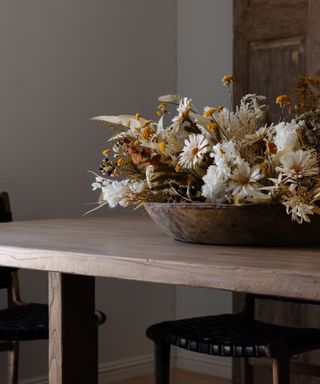 A rustic wooden table with a large bowl of dried flowers and stems
