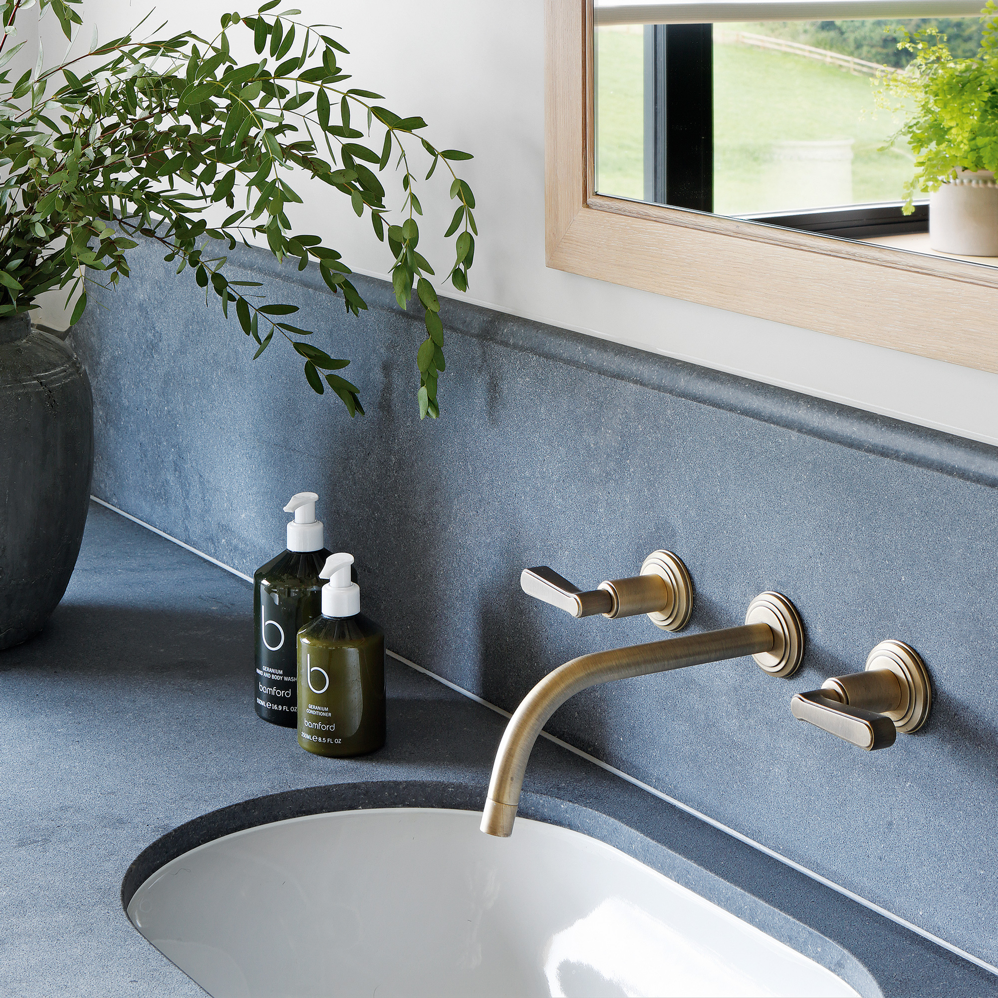 close up of a set of brass bathroom basin taps againts a concrete coloured quartz surround