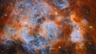 A swirling deep space nebula vista reveals pockets of pale blue glowing gas surrounded by reddish-orange clouds peppered with stars.