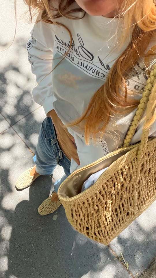 Courtney wears a graphic tee, jeans, raffia flats, and The Row's Georgica bag.