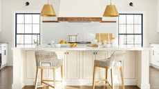 White kitchen with two large windows with black frames, a white subway tiled backsplash, an oven hood with wooden trim, a white kitchen island and walls painted in Benjamin Moore's Timid White.