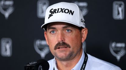 Keegan Bradley speaking at a press conference while wearing a white Srixon cap