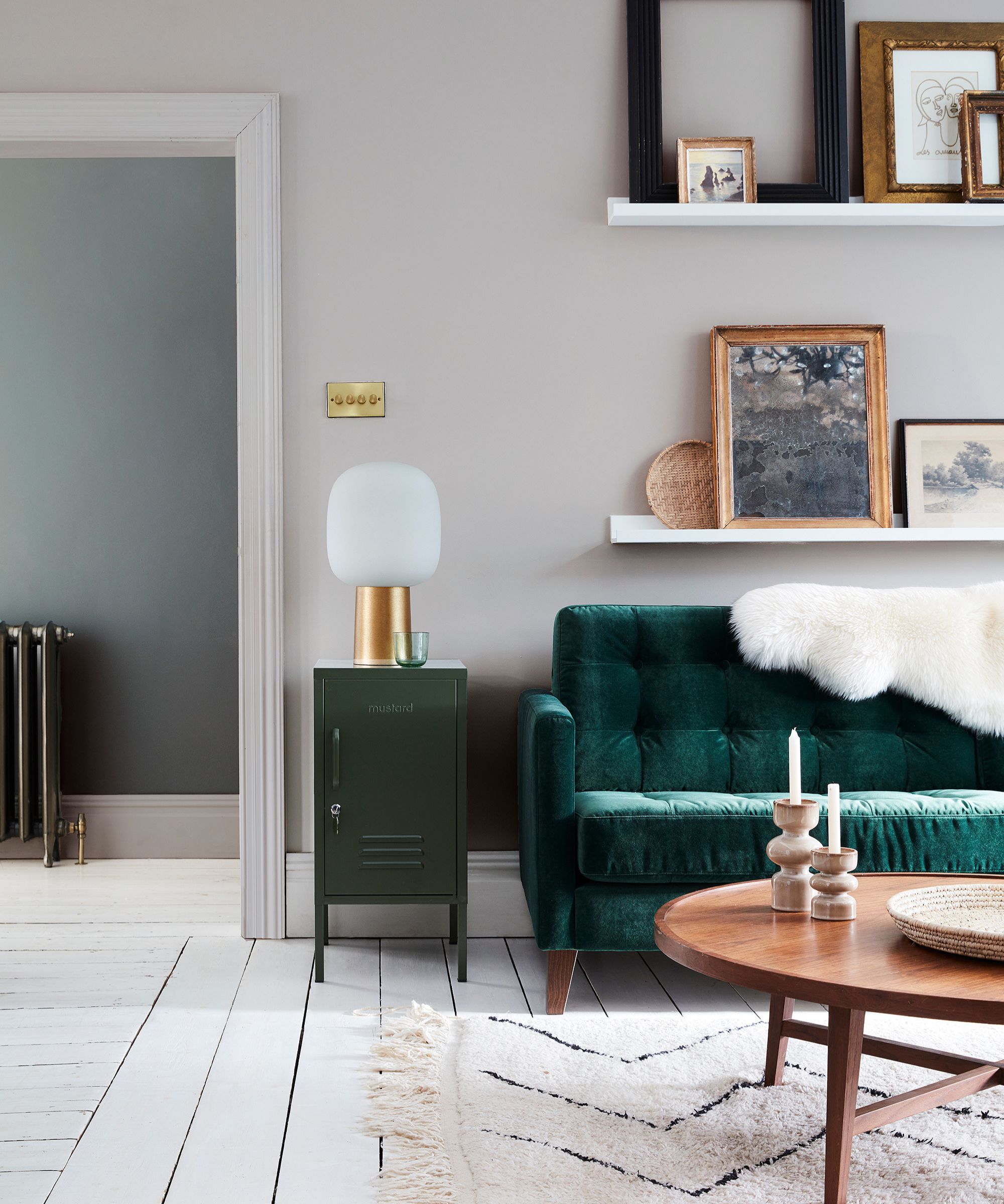 cozy living room with light gray walls, gallery shelves with artwork, and a dark green velvet sofa