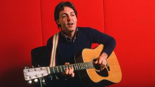 Portrait of British musician Paul McCartney as he plays acoustic guitar against a red background, October 7, 1984. 