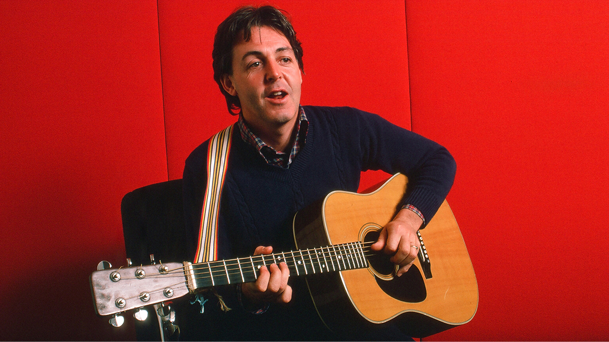 Portrait of British musician Paul McCartney as he plays acoustic guitar against a red background, October 7, 1984.