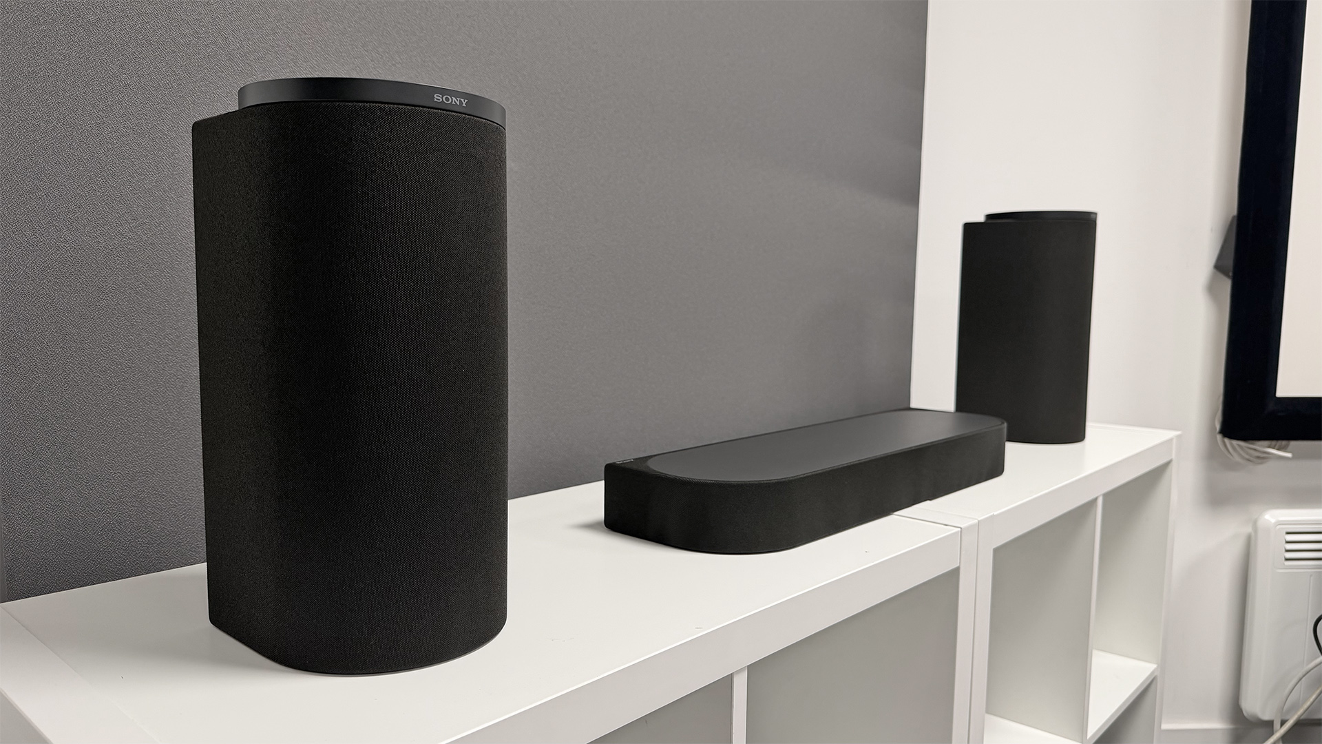 Sony Bravia Theatre Trio Dolby Atmos soundbar on white shelving unit in front of grey wall baffle