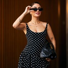 A woman at Paris Fashion Week wearing a black and white polka dot dress, black sunglasses, and black Chanel handbag.