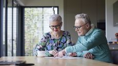 An older couple go over financial paperwork at their kitchen table.