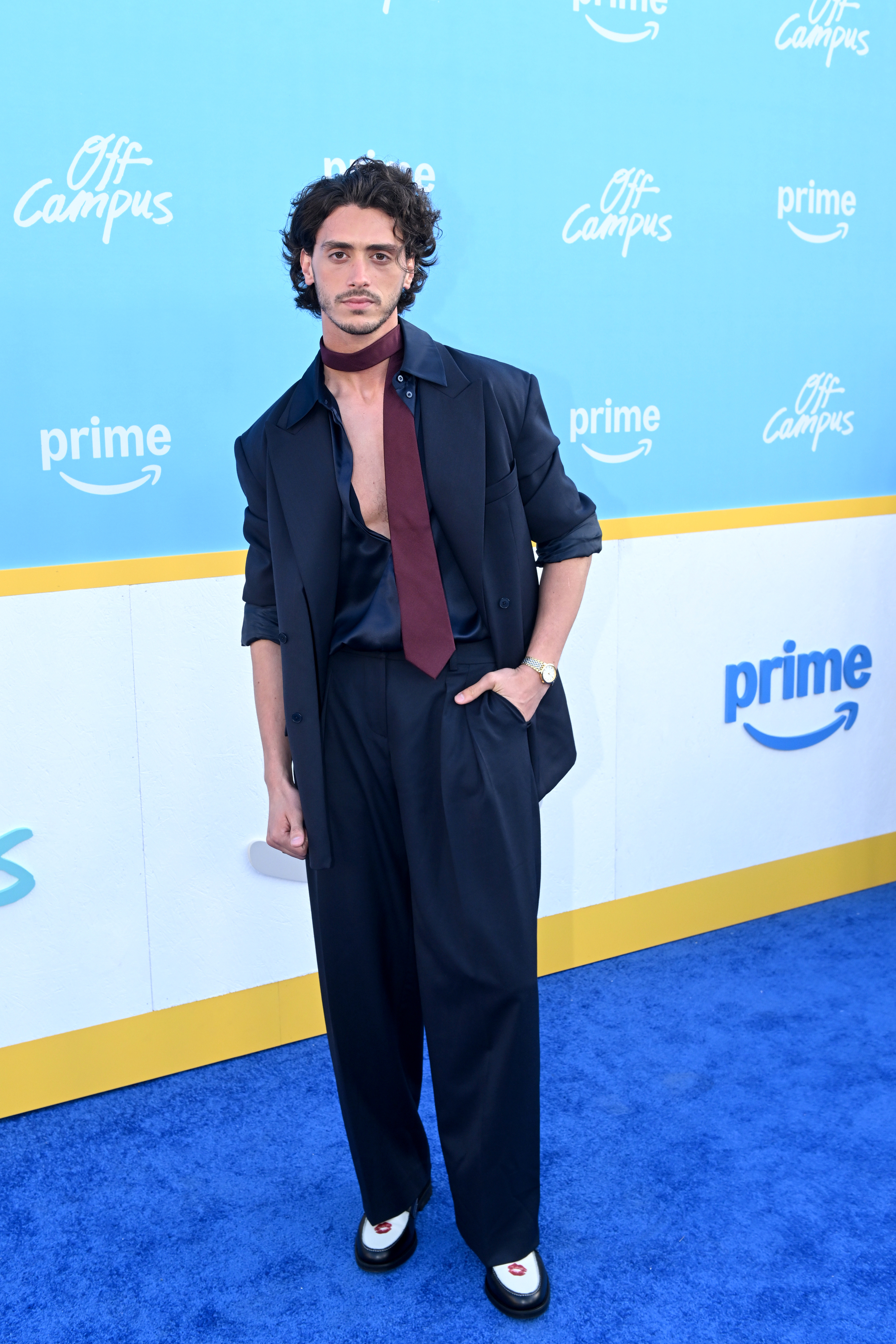 Antonio Cipriano who plays john logan wearing a blue suit and tie adjusted to the side on a carpet as he attends the "Off-Campus" Premiere and After-Party on April 29, 2026 in Los Angeles