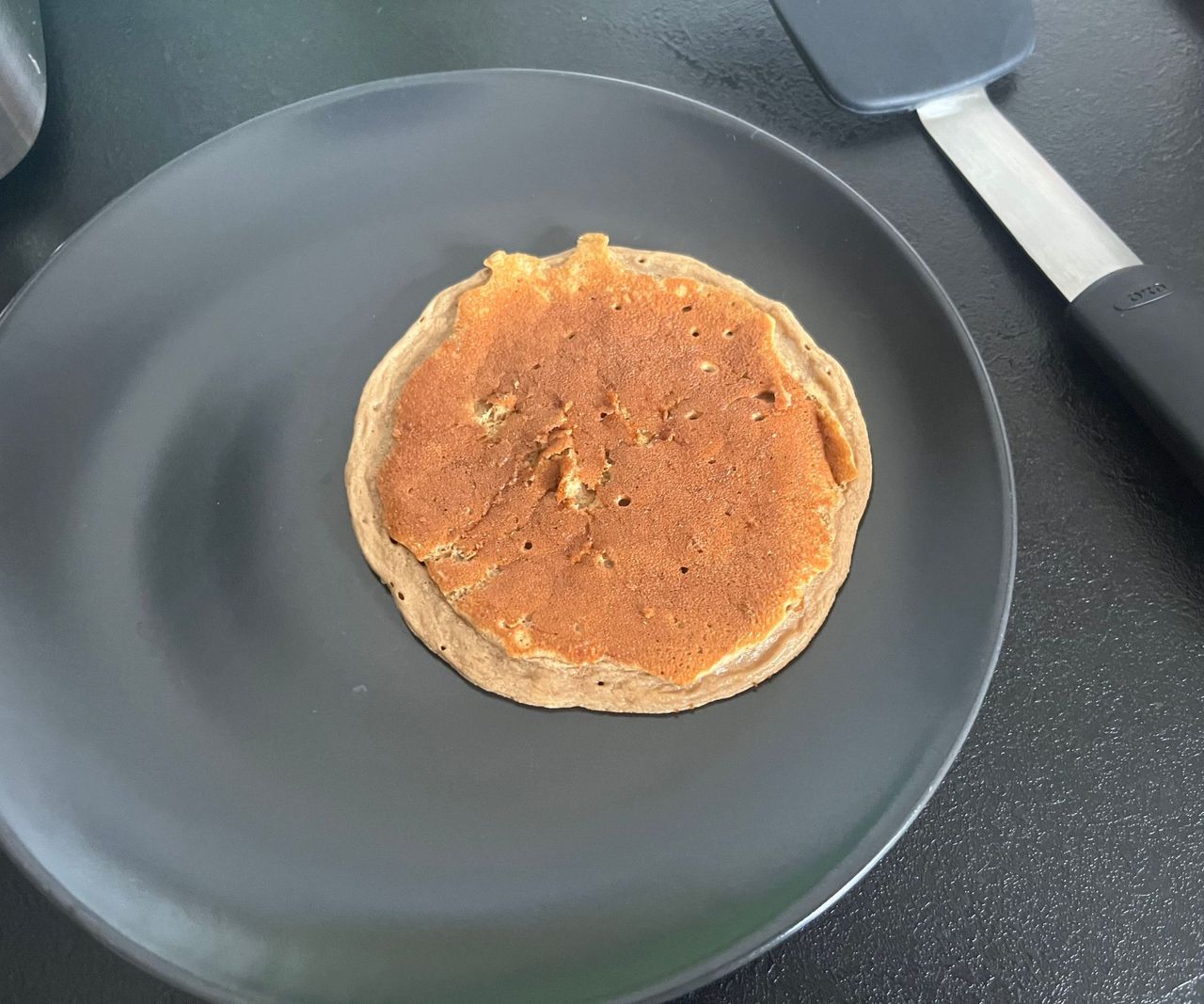 A golden pancake on a grey plate.