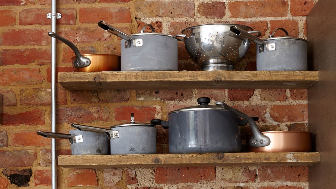 Open kitchen shelving displaying saucepans againast an exposed brick wall