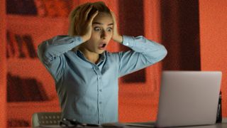 Young woman sitting in front of a laptop and looking shocked.