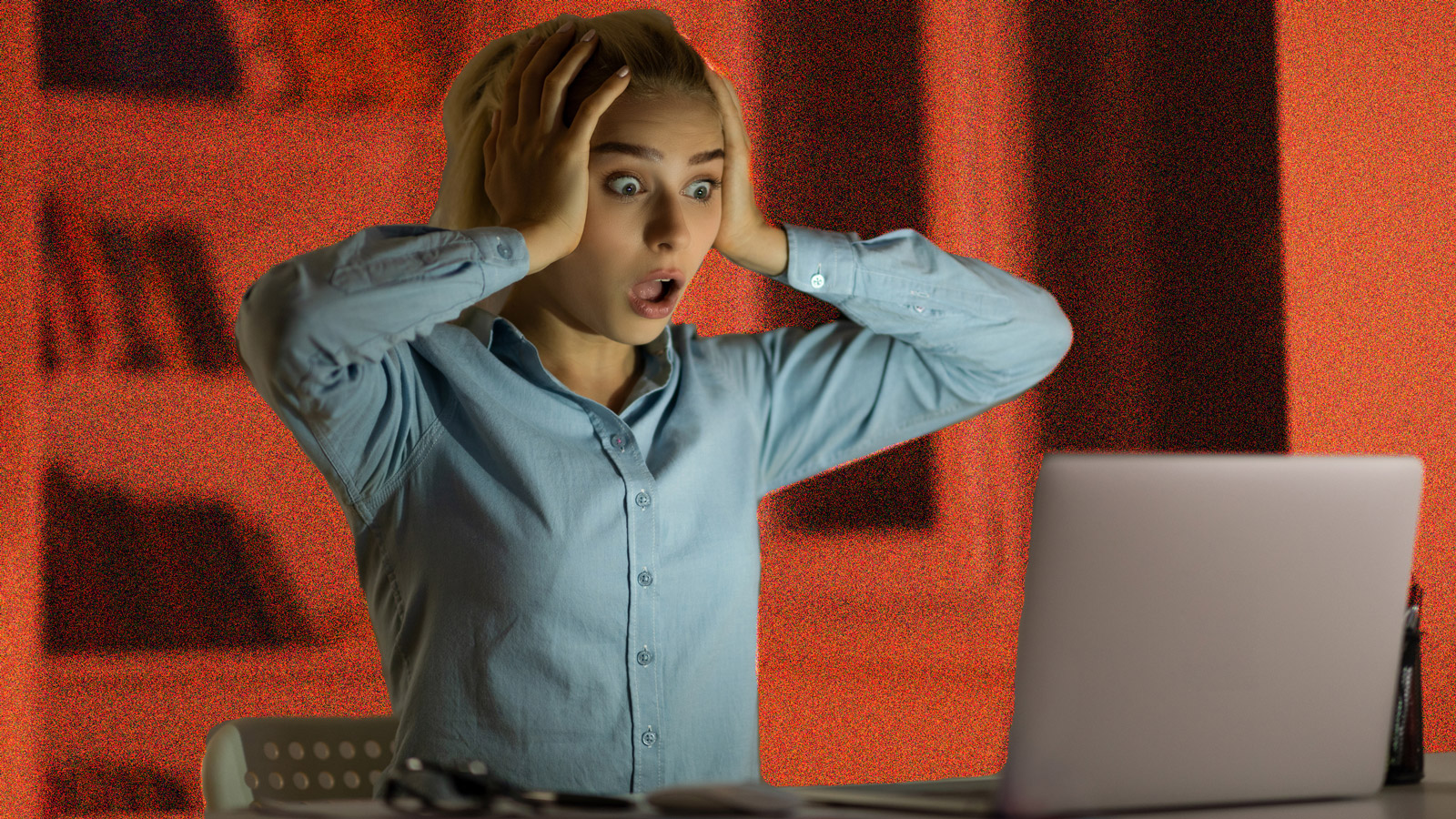 Young woman sitting in front of a laptop and looking shocked.
