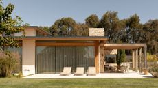 A beautiful home with an outdoor patio featuring sun loungers and a dining space under a pergola by a green lawn