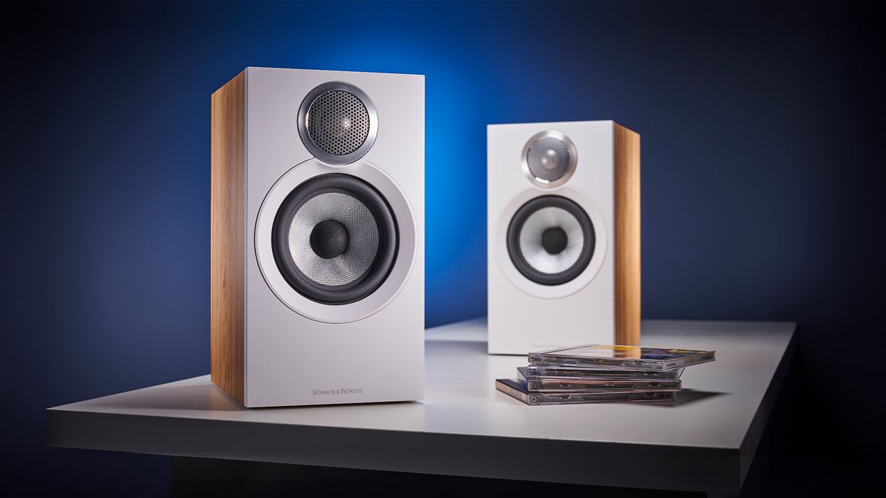 Bowers &amp; Wilkins 607 S3 in light oak finish against blue background with a stack of CDs in front