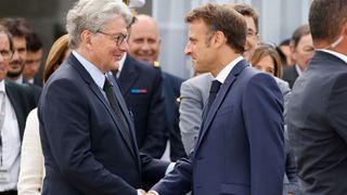 French President Emmanuel Macron (R) shakes hands with EU commissioner for internal market Thierry Breton as he visits the International Paris Air Show at the ParisLe Bourget Airport on June 19, 2023.