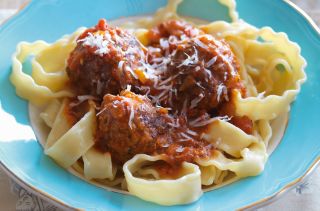 spaghetti and meatballs in a blue bowl dusted with cheese