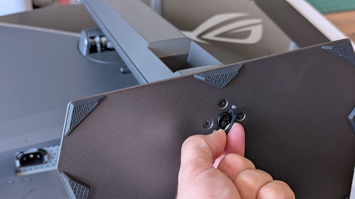 Hand tightening the ASUS ROG monitor stand screw, with the cable‑management section visible.