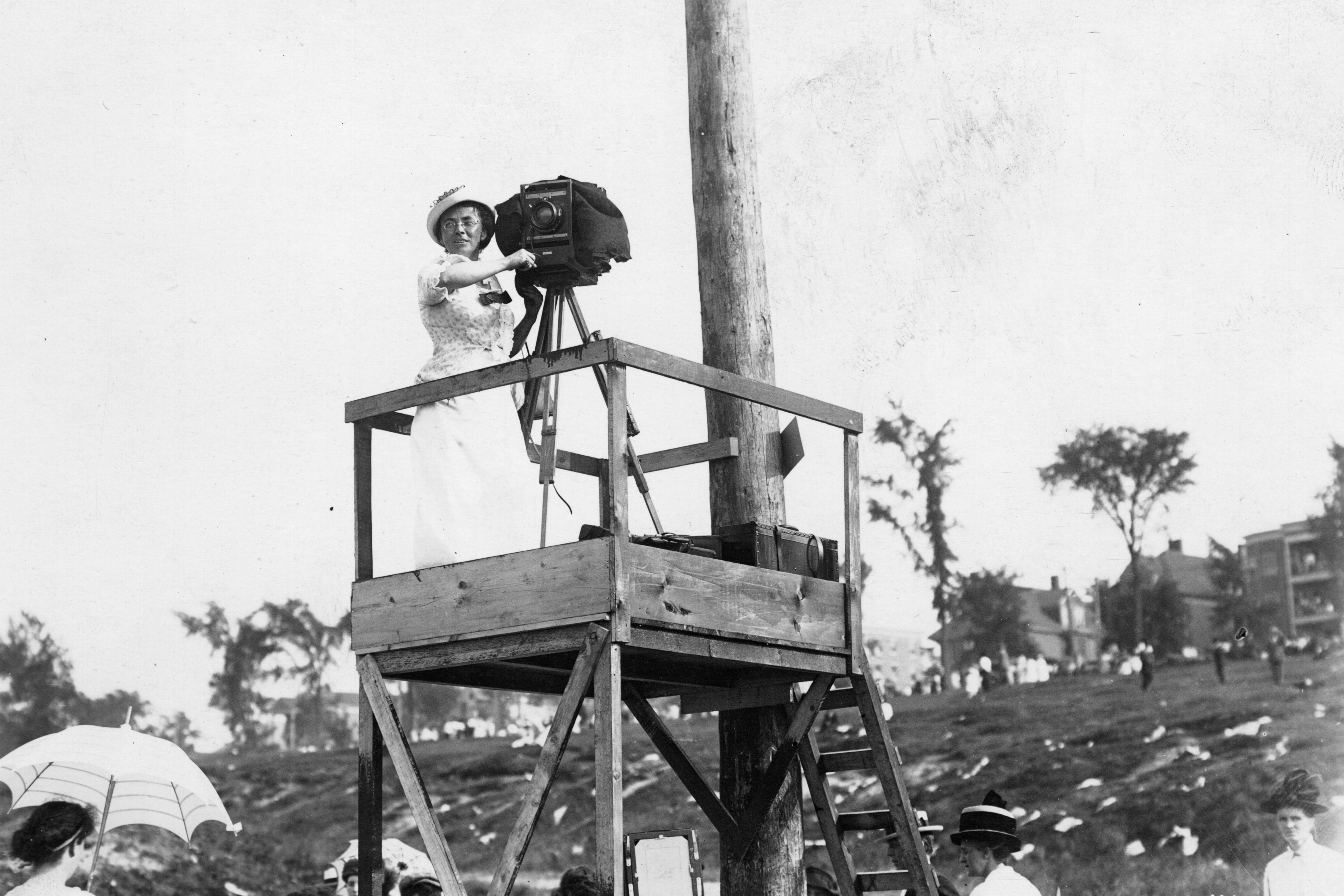 Close-up of photographer Jessie Tarbox Beals in white dress with camera on platform; other people walking about below, 1922. (Photo by Jessie Tarbox Beals/The New York Historical/Getty Images)