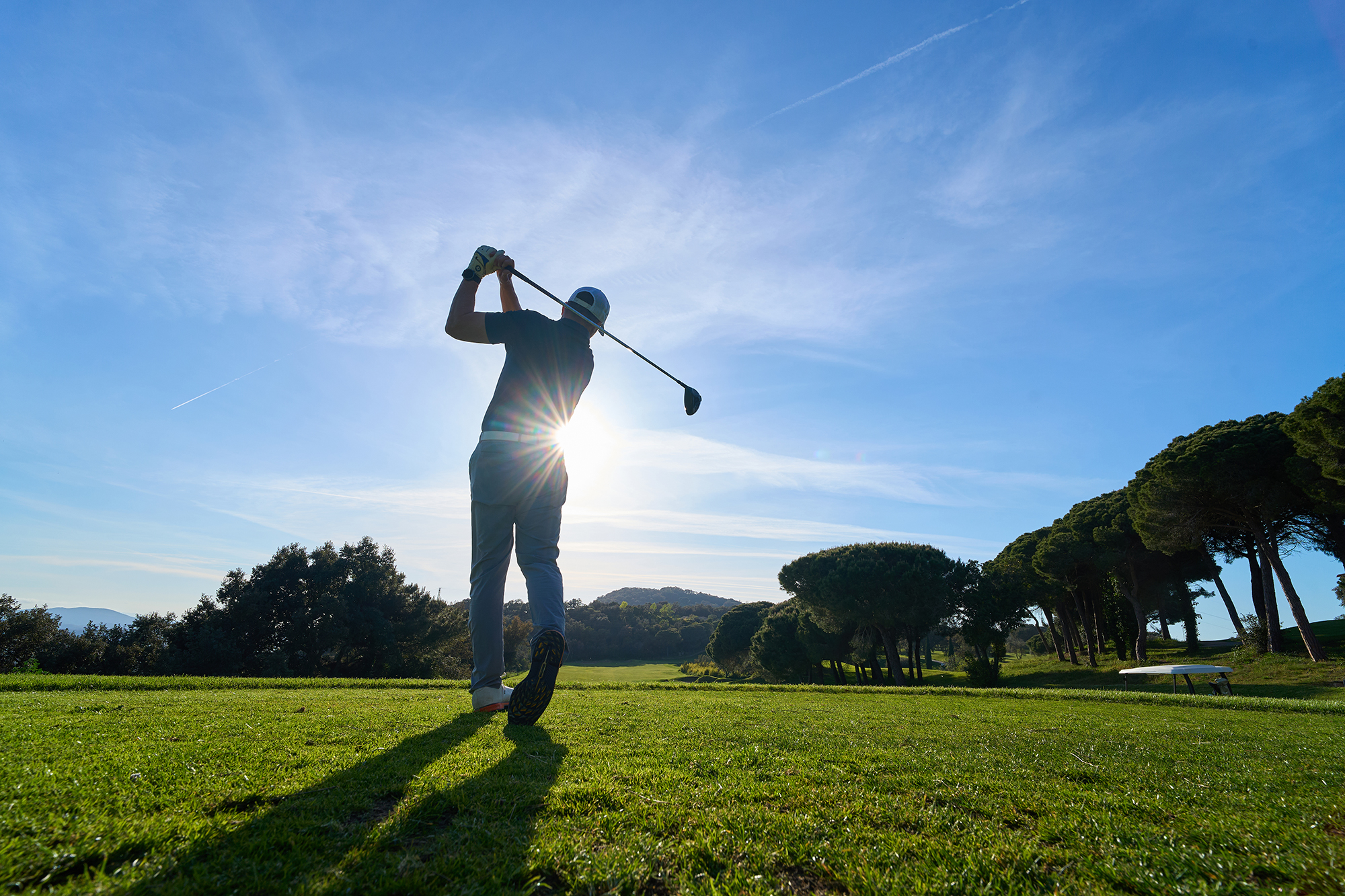 A male golfer in the finish position after hitting a tee shot with trees down the right hand side