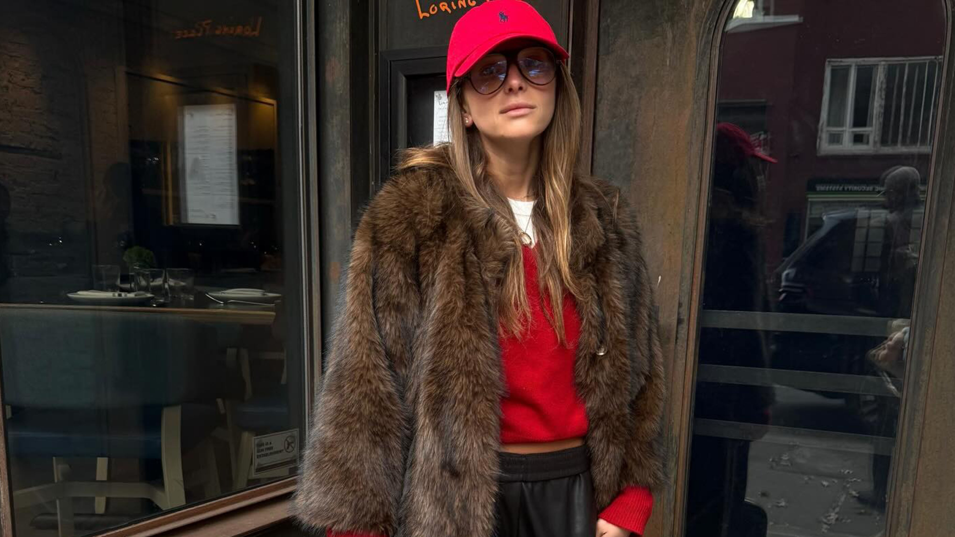 Woman in red cap, red sweater, faux-fur coat and black pants