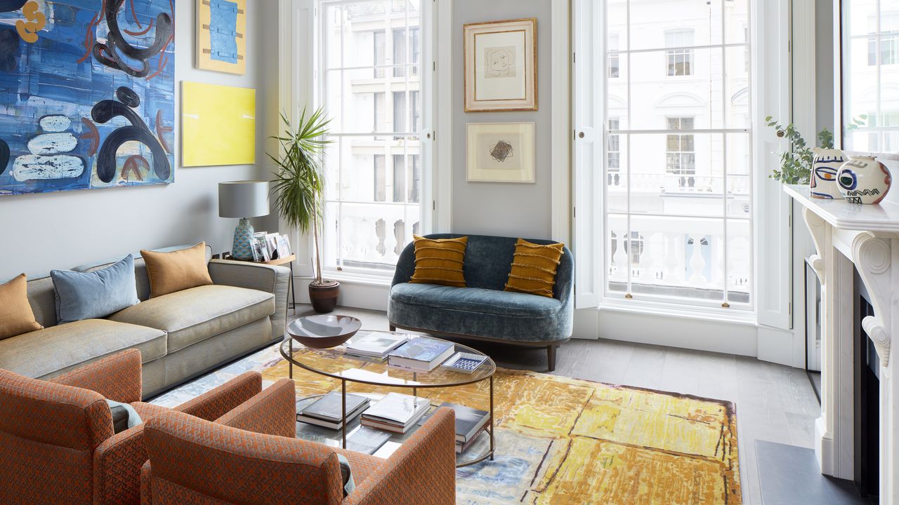 A drawing room with orange armchairs, a yellow and blue rug and contemporary pendant chandelier