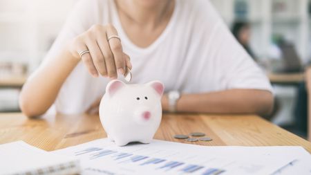 A woman puts a coin in a piggy bank.