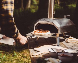 man taking pizza out of a tabletop pizza oven using a pizza paddle