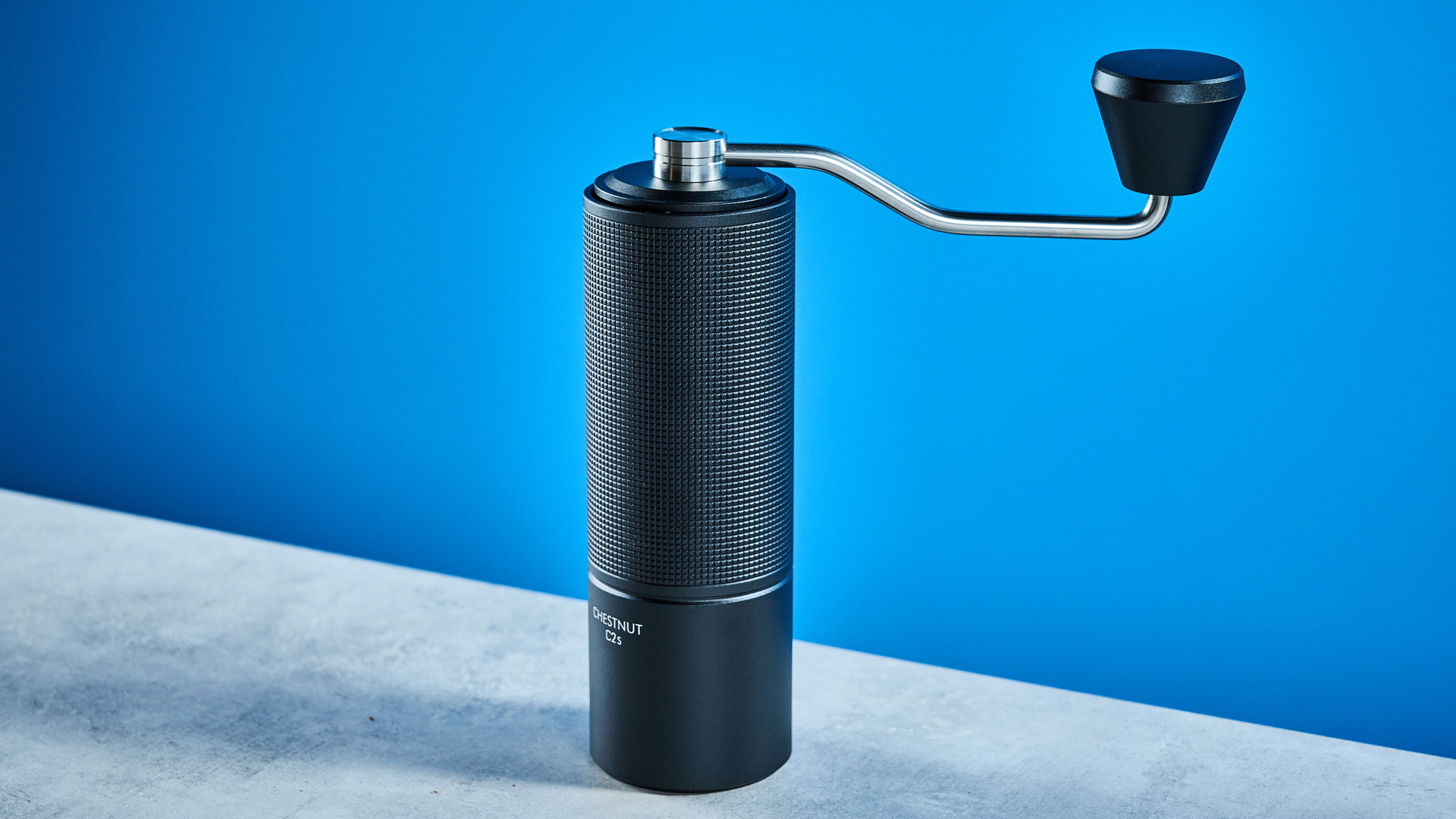 the timemore chestnut c2s coffee grinder in black showing its hand crank and catch chamber photographed against the blue tom's guide background