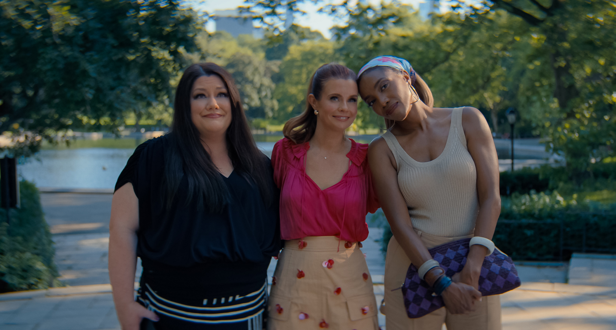 Brooke Elliott as Dana Sue Sullivan, JoAnna Garcia Swisher as Maddie Townsend, Heather Headley as Helen Decatur with their arms around each other in summer clothes smiling standing in a sunny central park in new york city