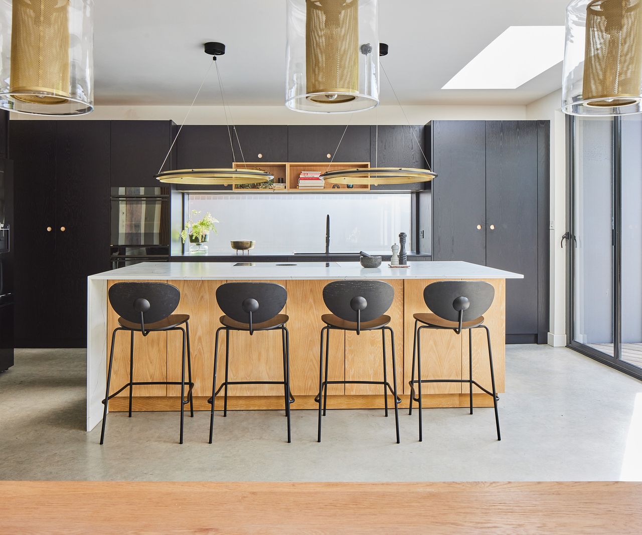 A modern kitchen in a self build home. There is a large central island of wood and stone with black kitchen cabinets.