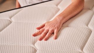 A hand rests against the surface of the Plank Firm mattress, Extra Firm side, testing the temperature regulation and pressure relief