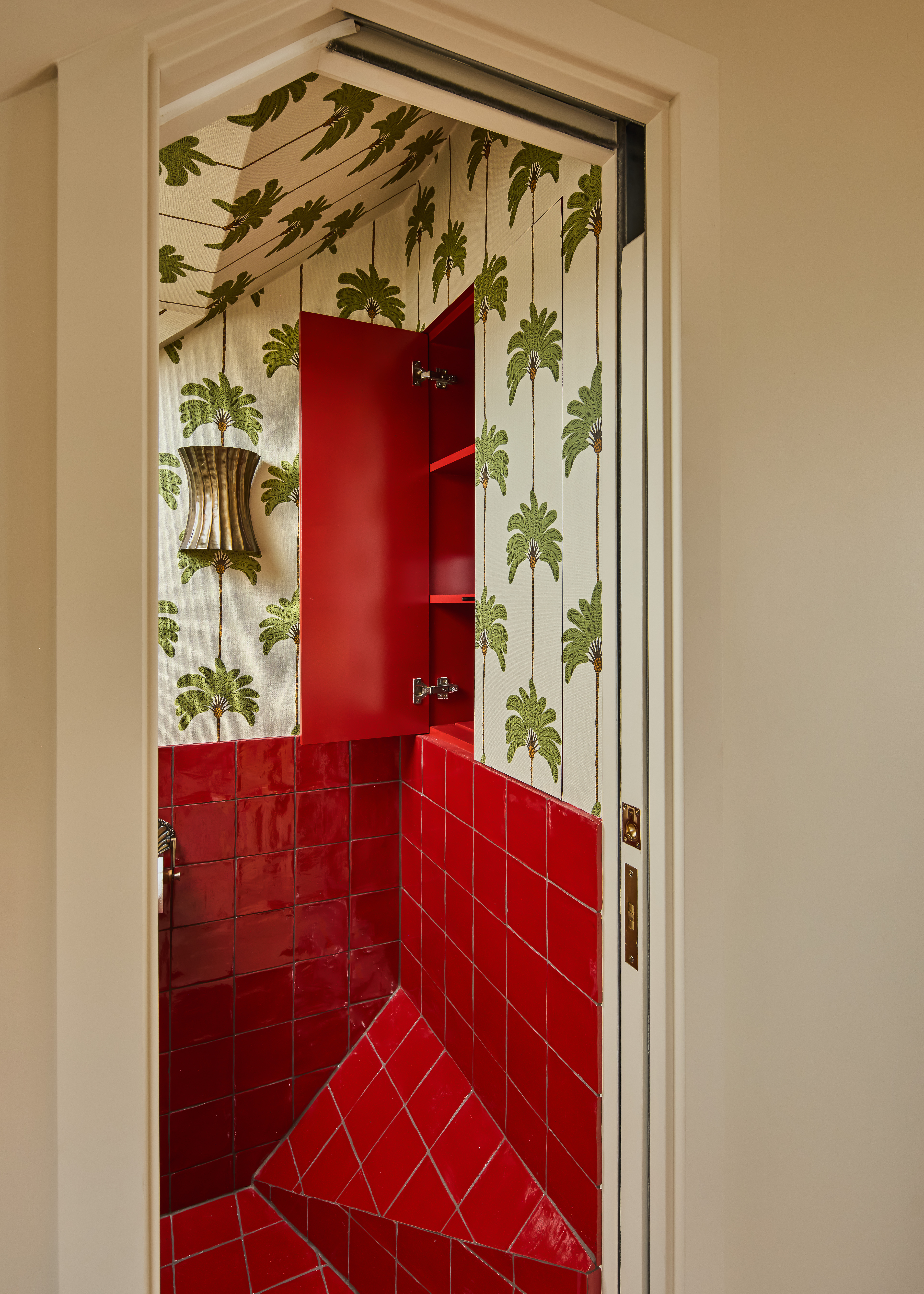 A red tiled bathroom with palm wallpaper and a hidden cabinet