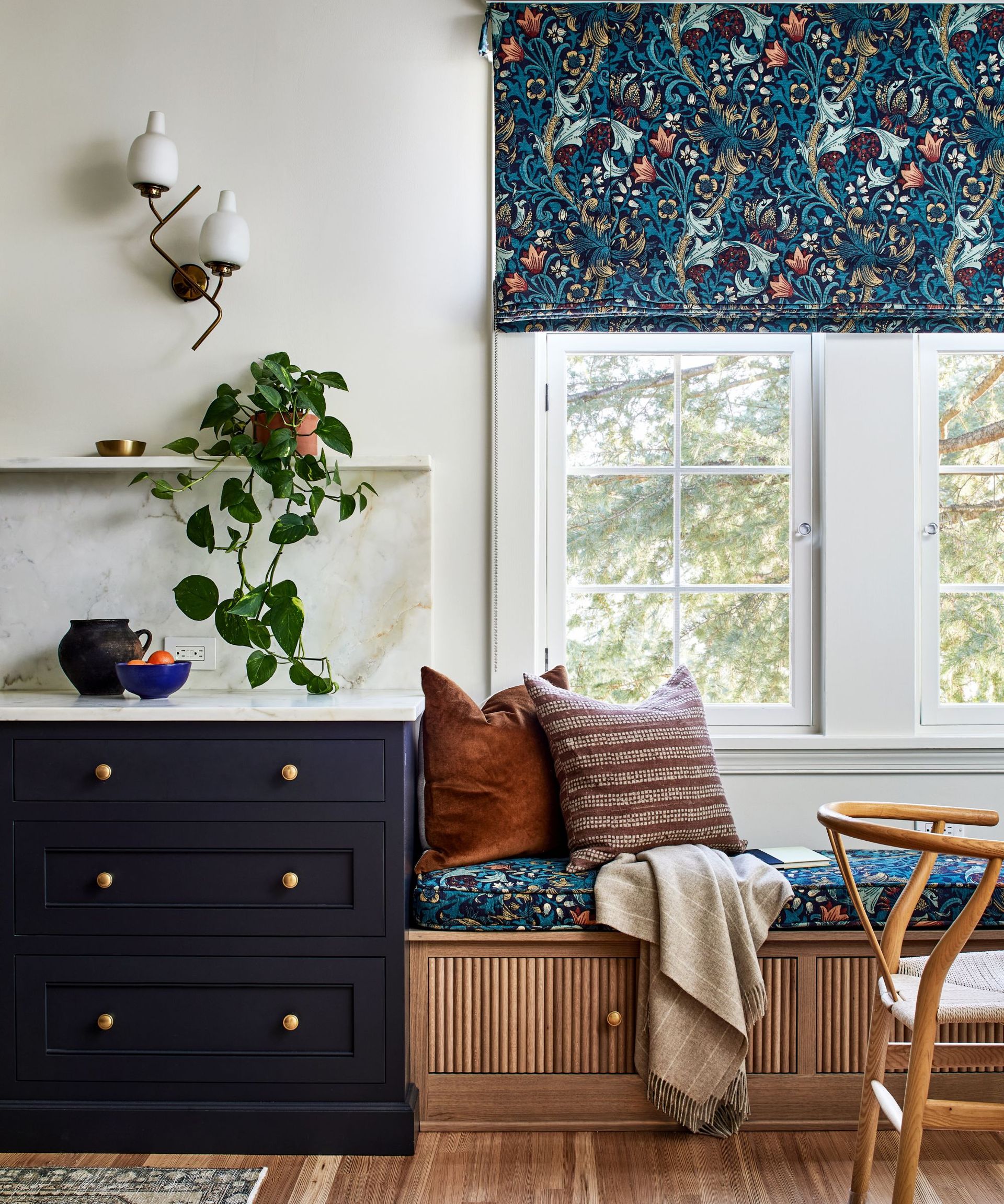A close up of a kitchen with dark blue cabinets and a dining nook with wood banquette seats and patterned throw pillows