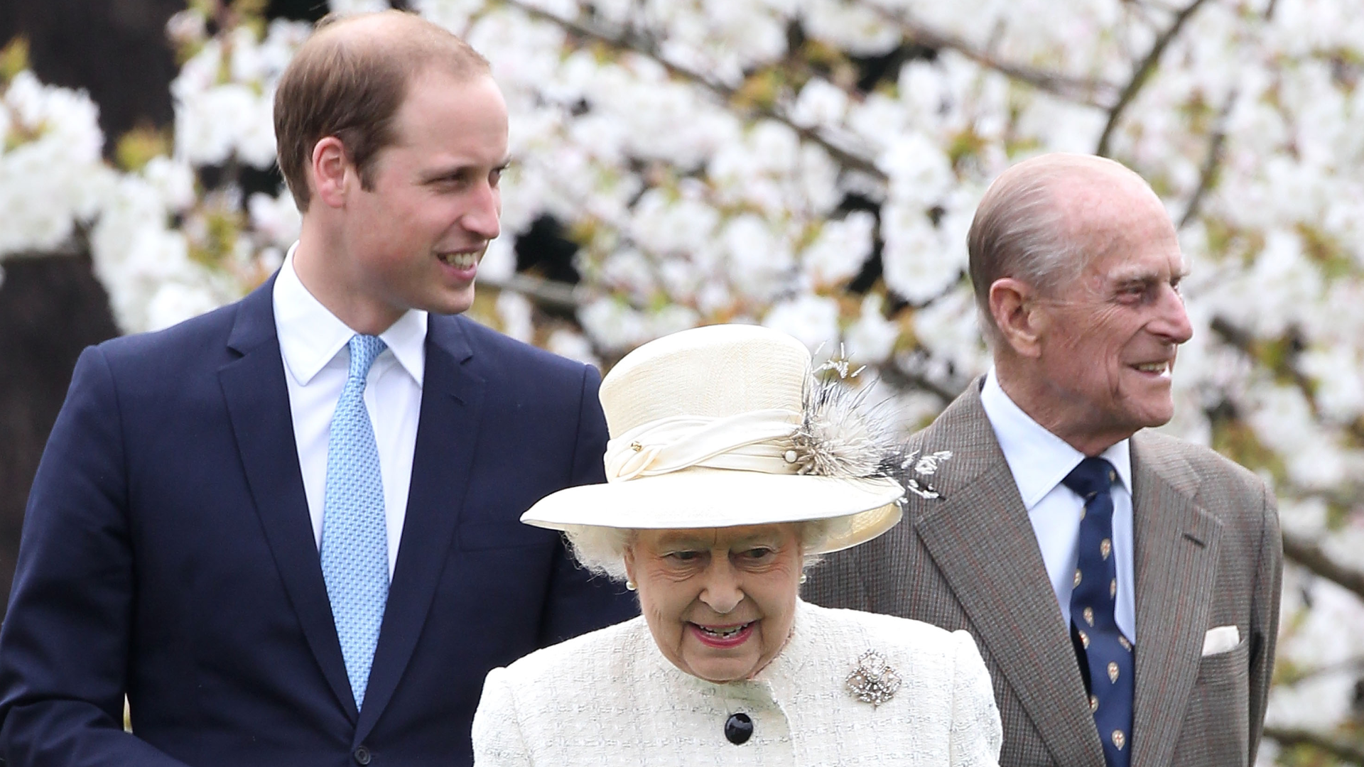 Prince William, Queen Elizabeth and Prince Philip standing in front of a flowering tree and smiling