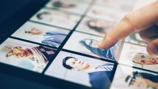 With only his finger showing, a man points at a photo of a woman among photos lined up on a tablet screen.
