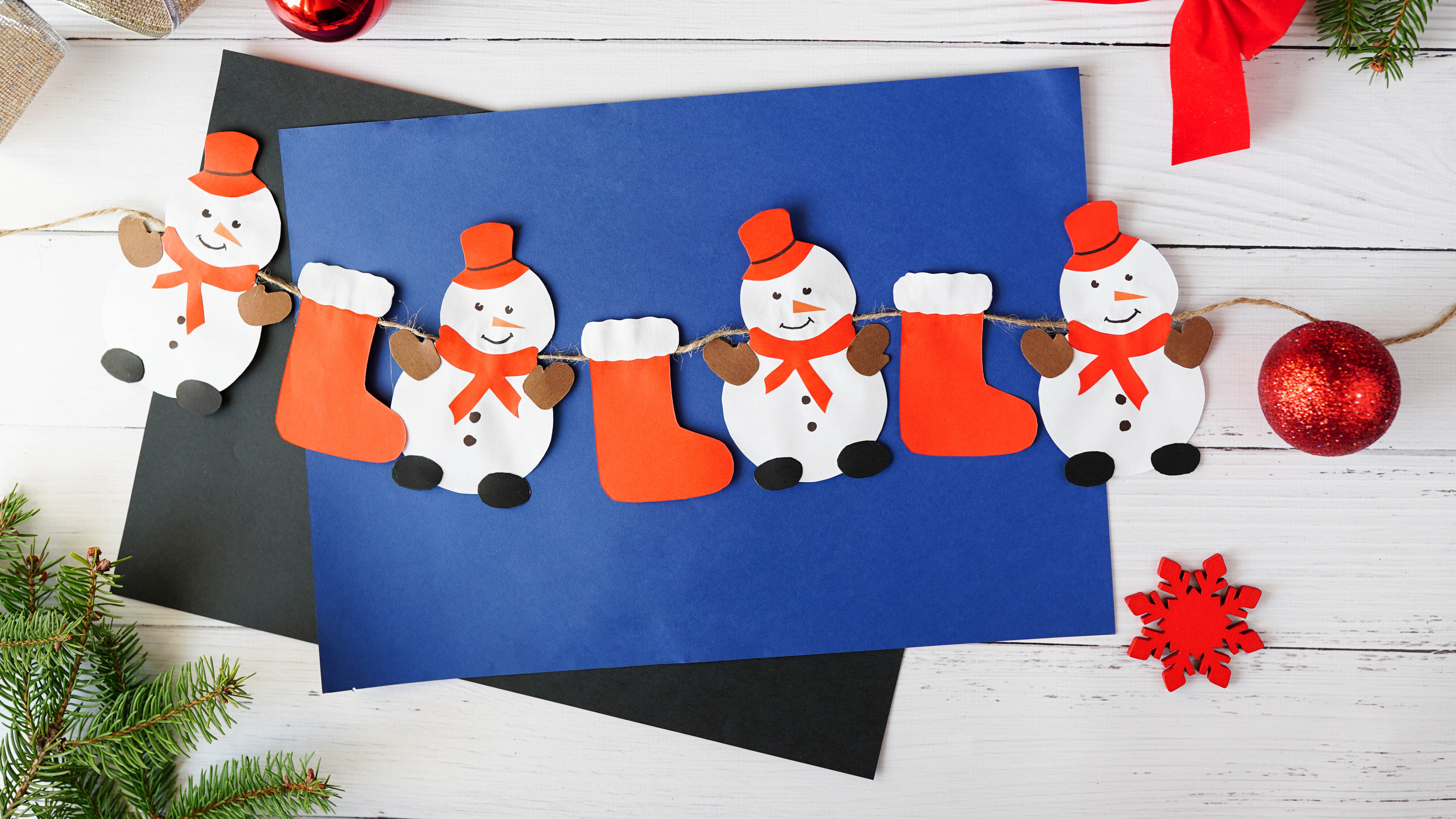 бумажная гирлянда из красных чулок и снеговиков на фоне синего конверта