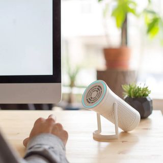 A white Wynd personal air purifier on a wooden desk next to a computer on a sunny day