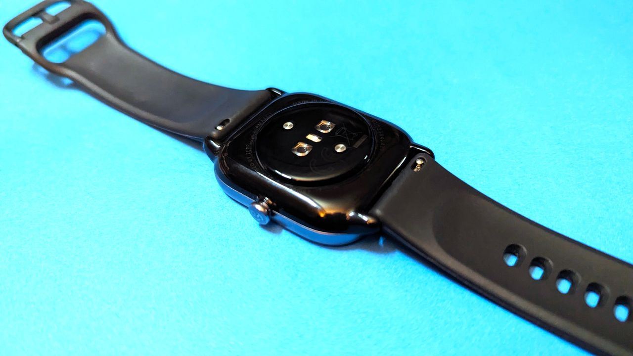 Amazfit GTS 4 Mini kept on a flat blue surface showcasing the back sensors and straps