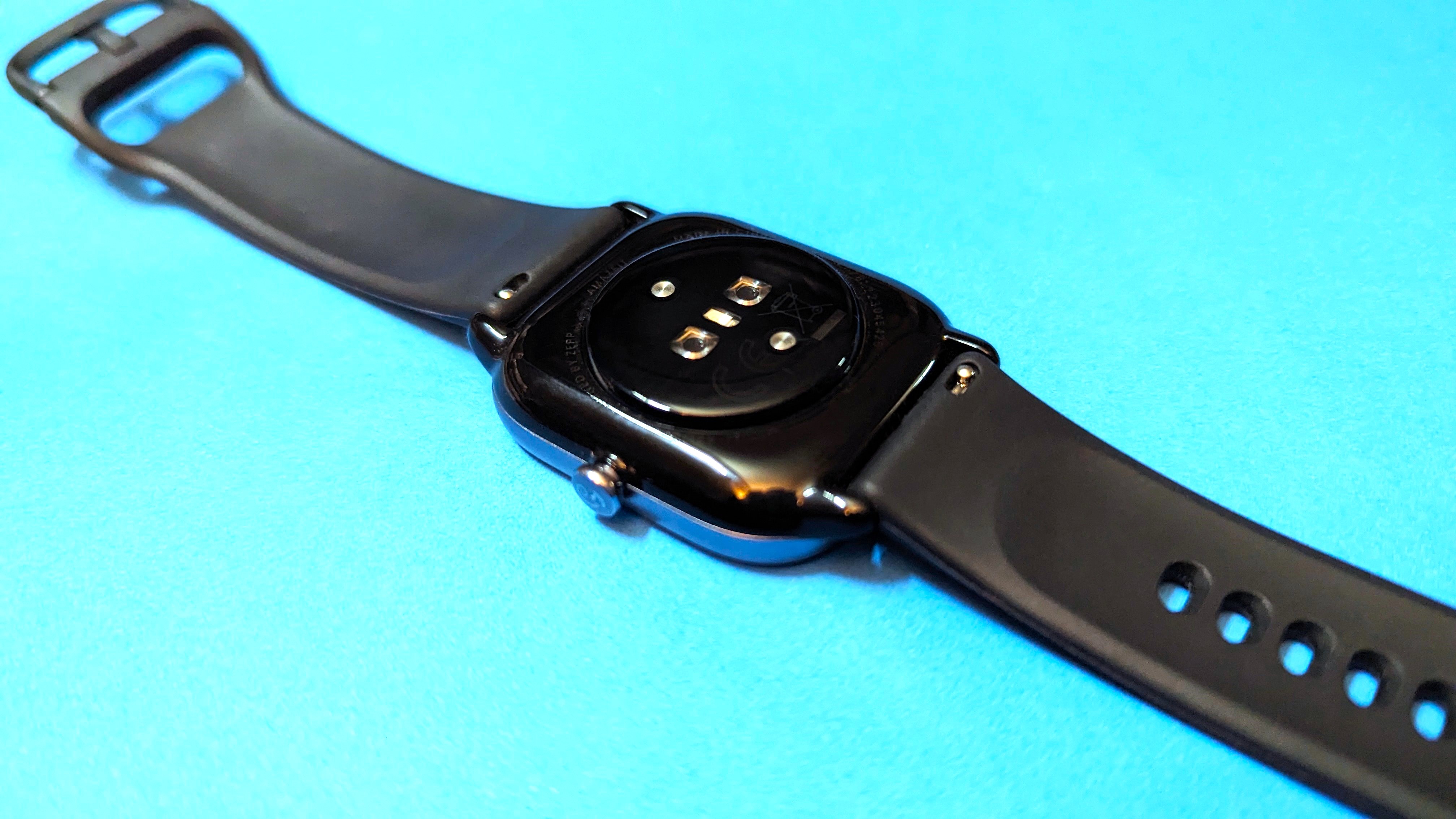 Amazfit GTS 4 Mini kept on a flat blue surface showcasing the back sensors and straps