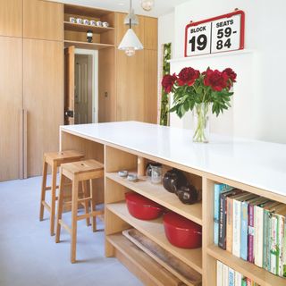 Wooden kitchen with wooden cabinets and matching kitchen island/breakfast bar, filled with cookbooks and cooking pots