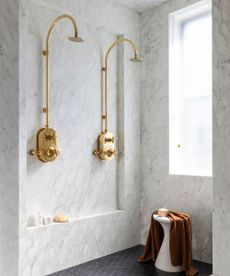 A walk-in shower with marble walls, black mosaic flooring, and who gold shower heads