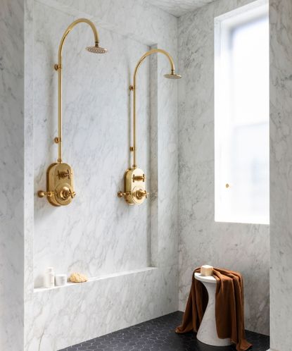 A walk-in shower with marble walls, black mosaic flooring, and who gold shower heads