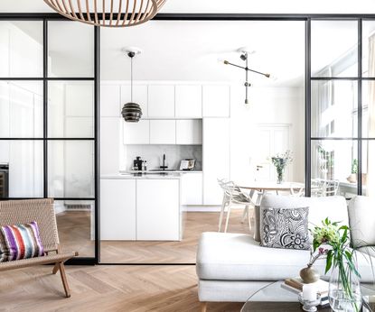 A white kitchen views through a black archway from a white living room