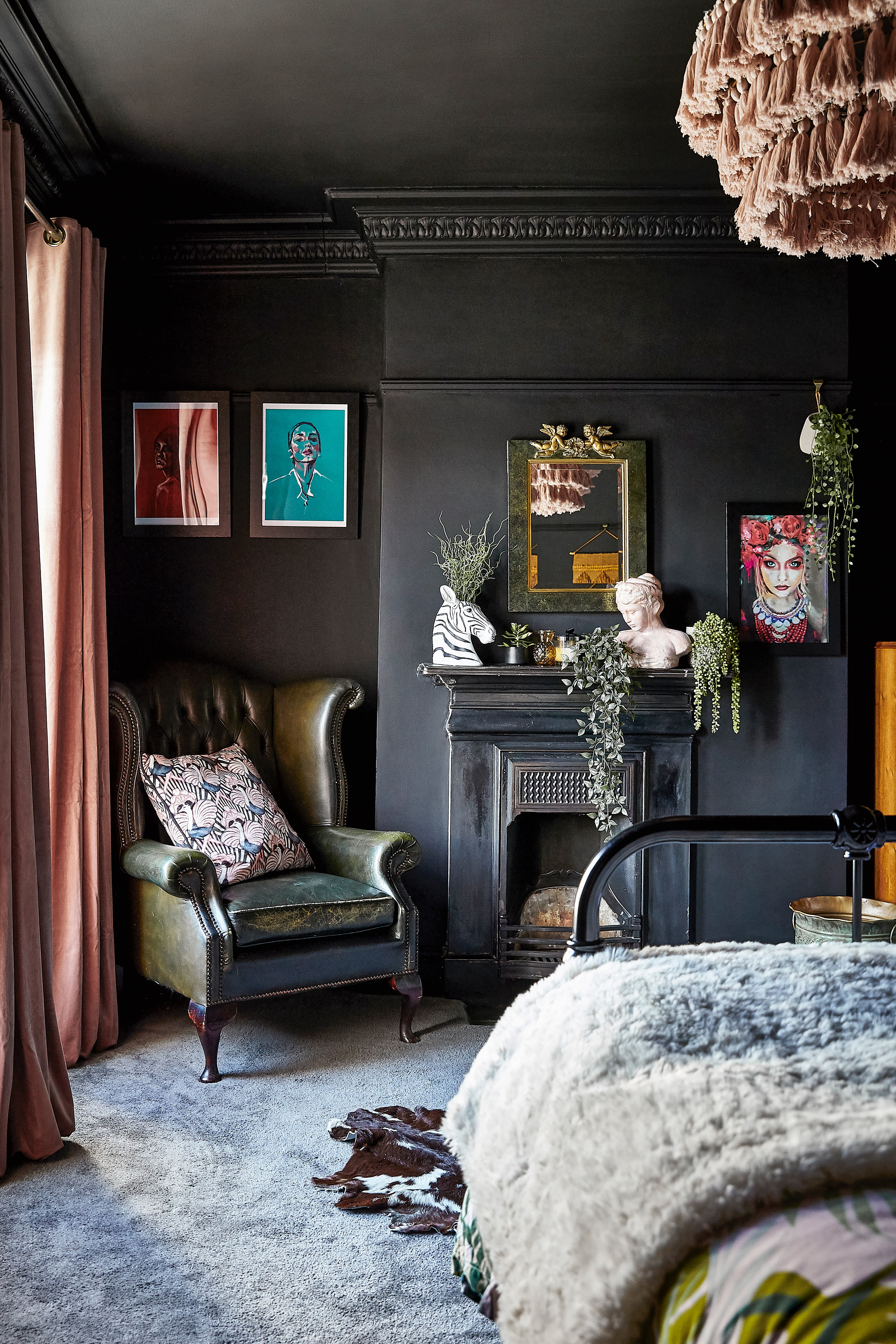 A black bedroom with painted walls and ceilings, framed wall art and and antique chair in corner