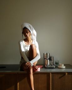 A woman sitting on the kitchen counter with her hair in a towel