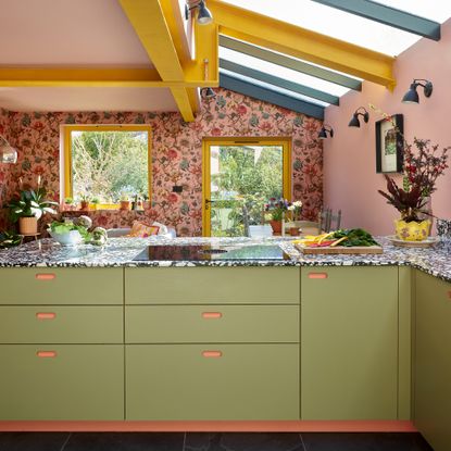 colourful kitchen with side extension pink ceiling yellow steel beams yellow framed window and glass door floral pink wallpaper and green kitchen cabinets with black and white worktop